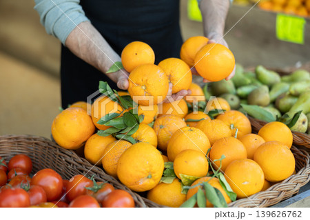 Male salesperson places oranges on display case. Closeup of salesperson hands and oranges Male salesperson places oranges on display case. Closeup of salesperson hands and oranges 139626762