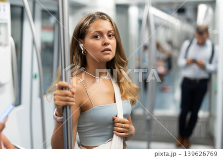 Young woman is standing in subway car with headphones Young woman is standing in subway car with headphones 139626769