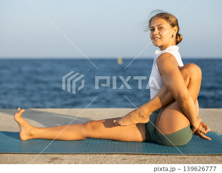 Sportive girl practicing seated yoga asana on seashore Sportive girl practicing seated yoga asana on seashore 139626777