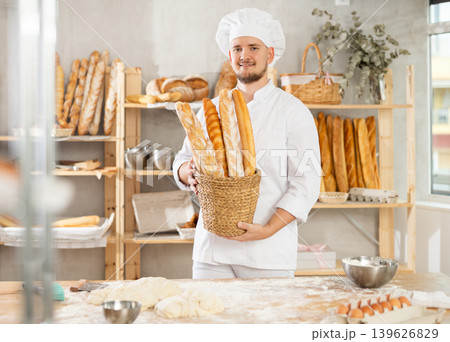 Male bakery employee offering different baguettes for sale Male bakery employee offering different baguettes for sale 139626829