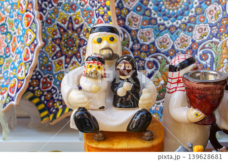 Doha, Qatar - Jan 14 2024, Close-up view of small ceramic statuettes in the form of an Arab man and woman with kids, in his arms, patterned dishes in the background, in Souq Waqif bazaar, Doha, Qatar Doha, Qatar - Jan 14 2024, Close-up view of small ceramic statuettes in the form of an Arab man and woman with kids, in his arms, patterned dishes in the background, in Souq Waqif bazaar, Doha, Qatar 139628681