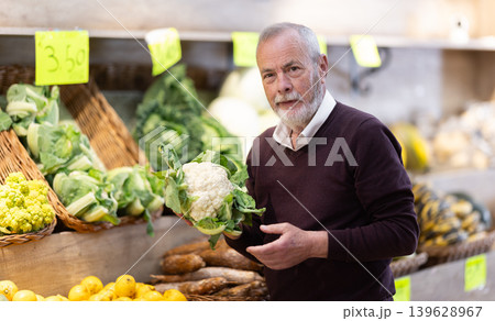 Elderly male customer buying fresh cauliflower in grocery store with assortment Elderly male customer buying fresh cauliflower in grocery store with assortment 139628967