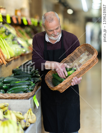Elderly owner of a farm store holds a zucchini in hands Elderly owner of a farm store holds a zucchini in hands 139628987