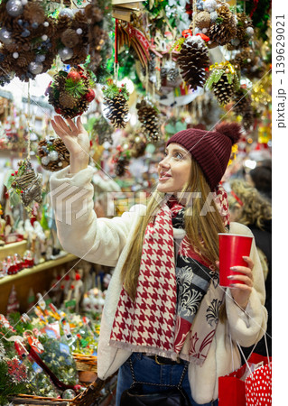 Young woman in souvenir shop examines Christmas handmade toys Young woman in souvenir shop examines Christmas handmade toys 139629021