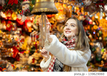 Young girl chooses festive New Year decorations for house and examines bell. Young girl chooses festive New Year decorations for house and examines bell. 139629060