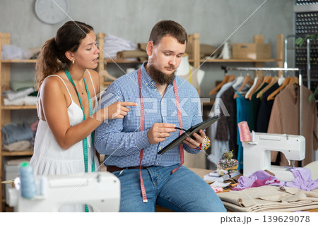 Young dressmakers sketching on tablet together in sewing workshop Young dressmakers sketching on tablet together in sewing workshop 139629078