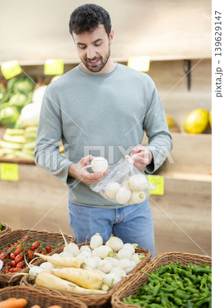 Man is standing in a supermarket and choosing a white turnip Man is standing in a supermarket and choosing a white turnip 139629147