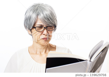 黒ぶちの老眼鏡をかけてしかめっ面で読書をする老眼が進んだシニア女性 黒ぶちの老眼鏡をかけてしかめっ面で読書をする老眼が進んだシニア女性 139629708
