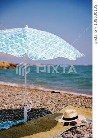Beach umbrella with hat and sunglasses on pebble beach in summer Beach umbrella with hat and sunglasses on pebble beach in summer 139630135