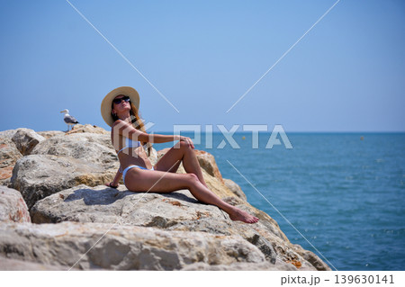 Woman sunbathing on seaside rocks in bikini during summer vacation Woman sunbathing on seaside rocks in bikini during summer vacation 139630141