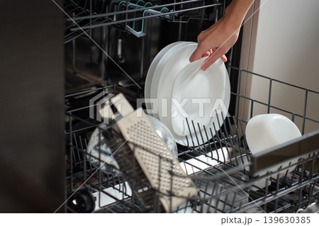 Hand loading white plate into open dishwasher rack Hand loading white plate into open dishwasher rack 139630385