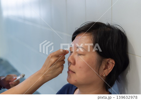 Woman applying eyebrow makeup with cosmetic brush during beauty routine featuring skincare grooming and personal care in indoor setting Woman applying eyebrow makeup with cosmetic brush during beauty routine featuring skincare grooming and personal care in indoor setting 139632978