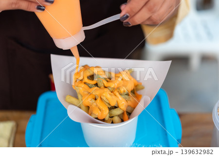 Closeup of crispy french fries topped with creamy cheese sauce in paper cup prepared by street food vendor with casual fast food presentation Closeup of crispy french fries topped with creamy cheese sauce in paper cup prepared by street food vendor with casual fast food presentation 139632982