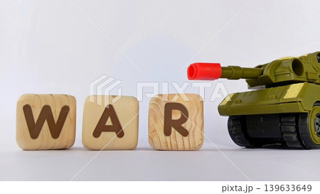 The text "WAR" on a cube or wooden block with miniature tanks and war trucks. World war illustration. 139633649