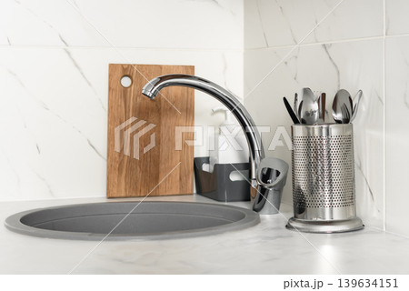 Modern kitchen sink with chrome faucet and utensils holder Modern kitchen sink with chrome faucet and utensils holder 139634151