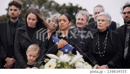 Funeral, cemetery and family with American flag for veteran for respect, ceremony and memorial service. Sad, depression and people by coffin in graveyard for military hero, army and soldier mourning 139634555