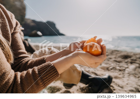 Tangerine hands beach woman holds a fresh citrus fruit while sitting on a pebble shore by the sea on a sunny day 139634965