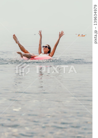 Woman inflatable ocean splashes in calm sea water with arms raised while enjoying a sunny summer vacation at the beach Woman inflatable ocean splashes in calm sea water with arms raised while enjoying a sunny summer vacation at the beach 139634979