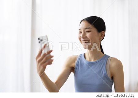 スマートフォンでビデオ通話しながら微笑むヨガウェアを着た日本人女性 スマートフォンでビデオ通話しながら微笑むヨガウェアを着た日本人女性 139635313