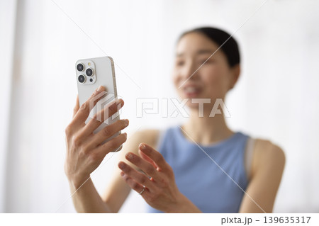 スマートフォンでビデオ通話しながら微笑むヨガウェアを着た日本人女性 スマートフォンでビデオ通話しながら微笑むヨガウェアを着た日本人女性 139635317