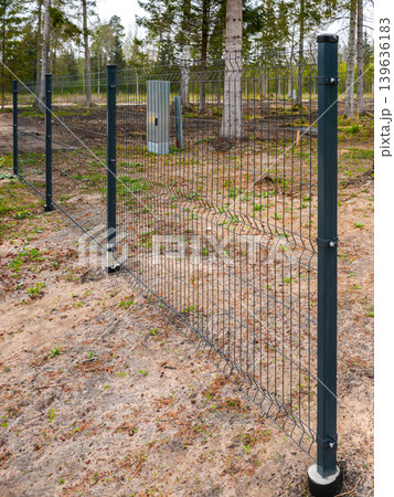 Metal mesh security fence, steel posts fixed in concrete-filled pipes buried in the ground Metal mesh security fence, steel posts fixed in concrete-filled pipes buried in the ground 139636183