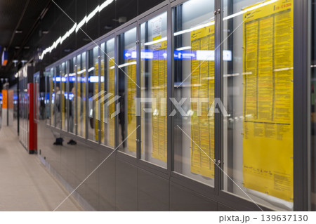 Public transport schedules are printed on yellow paper inside glass cabinets at a modern railway station to assist passengers with travel information, commuter logistics, and urban navigation 139637130