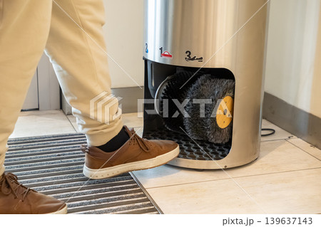 A professional person uses an automatic shoe polisher machine with rotating bristles in an office lobby to maintain leather footwear cleanliness and look sharp in a modern corporate setting 139637143