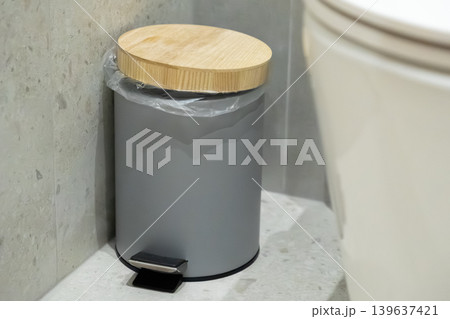Modern grey pedal bin with a wooden lid in a minimalist bathroom, highlighting functional interior design and efficient waste management solutions for a clean contemporary residence 139637421