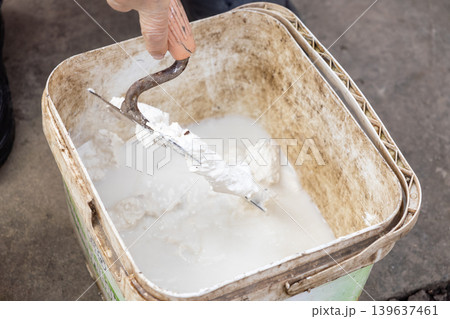 Trowel mixing white mortar in a plastic bucket on a construction site, emphasizing professional renovation preparation, manual labor, home improvement, and building material craft Trowel mixing white mortar in a plastic bucket on a construction site, emphasizing professional renovation preparation, manual labor, home improvement, and building material craft 139637461