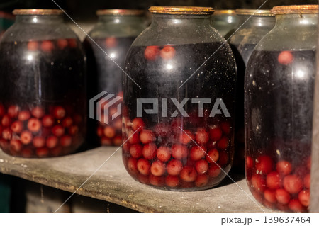 Glass jars filled with homemade preserved cherries sit on a rustic wooden cellar shelf, showcasing traditional canning methods and essential long-term food supplies for the winter Glass jars filled with homemade preserved cherries sit on a rustic wooden cellar shelf, showcasing traditional canning methods and essential long-term food supplies for the winter 139637464