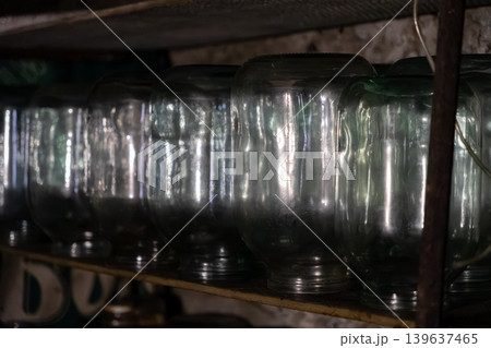 Row of empty glass jars lined up on a wooden shelf in a dark pantry, highlighting home food preservation, rustic kitchen storage solutions, and traditional rural life preparation Row of empty glass jars lined up on a wooden shelf in a dark pantry, highlighting home food preservation, rustic kitchen storage solutions, and traditional rural life preparation 139637465
