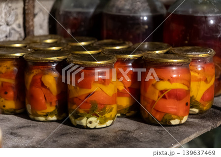 Glass jars with preserved bell peppers and spices sit on a rustic cellar shelf, representing homemade food supplies, traditional culinary methods, and sustainable pantry storage 139637469