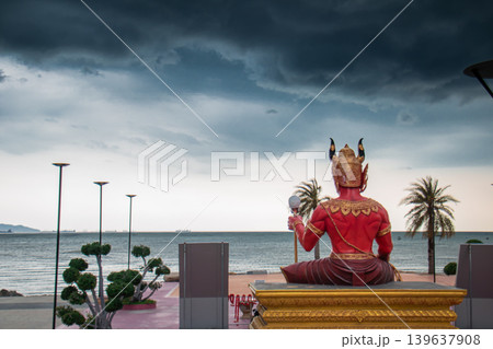 Seaside statue facing ocean under dramatic storm sky with palm tree, calm water, and promenade at sunset 139637908