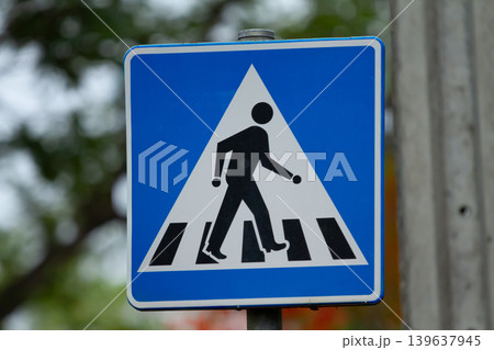 Pedestrian crossing sign with blue background and white triangle on outdoor street post 139637945