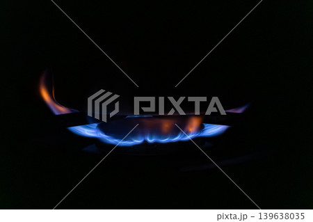 Blue gas flame burning on a kitchen stove burner under a pot, highlighting energy consumption and culinary preparation in a home environment with dramatic dark moody lighting Blue gas flame burning on a kitchen stove burner under a pot, highlighting energy consumption and culinary preparation in a home environment with dramatic dark moody lighting 139638035