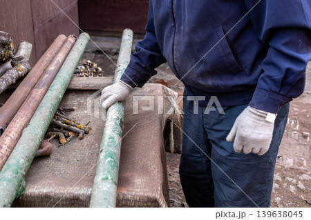 A manual worker wearing protective gloves holds a metal pipe on a workbench for an industrial construction or renovation project, highlighting professional labor, maintenance, and craft A manual worker wearing protective gloves holds a metal pipe on a workbench for an industrial construction or renovation project, highlighting professional labor, maintenance, and craft 139638045