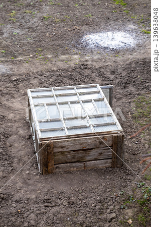 Rustic wooden cold frame box with glass window lid placed in soil, representing sustainable urban gardening, early spring seedling protection, and traditional small scale vegetable farming 139638048