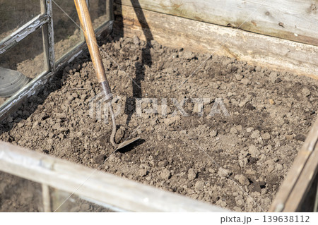 Old hand hoe resting in dark soil inside a wooden garden cold frame, reflecting rural spring preparation and organic vegetable cultivation for sustainable food growth in a backyard setting Old hand hoe resting in dark soil inside a wooden garden cold frame, reflecting rural spring preparation and organic vegetable cultivation for sustainable food growth in a backyard setting 139638112