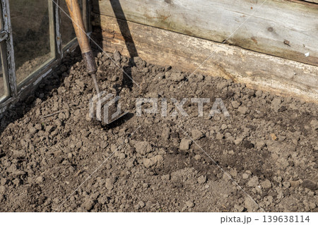 An old metal hoe stands in dark fertile soil inside a wooden greenhouse, preparing the ground for planting seeds and nurturing organic growth during the spring season for a vegetable garden An old metal hoe stands in dark fertile soil inside a wooden greenhouse, preparing the ground for planting seeds and nurturing organic growth during the spring season for a vegetable garden 139638114