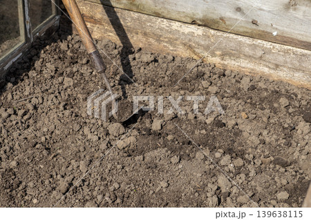 An old metal hoe digs into rich dark soil inside a rustic garden bed to prepare land for spring planting, symbolizing sustainable agriculture, hobby farming, and manual labor in horticulture An old metal hoe digs into rich dark soil inside a rustic garden bed to prepare land for spring planting, symbolizing sustainable agriculture, hobby farming, and manual labor in horticulture 139638115