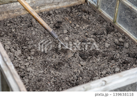 An old metal hoe rests inside a wooden garden frame with loose soil, representing traditional agricultural work, seasonal planting preparation, and organic hobby farming in a backyard vegetable patch An old metal hoe rests inside a wooden garden frame with loose soil, representing traditional agricultural work, seasonal planting preparation, and organic hobby farming in a backyard vegetable patch 139638118