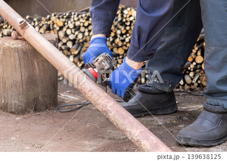 A professional worker uses a powerful electric angle grinder to clean thick rust from a metal pipe, showcasing industrial craftsmanship and skilled manual labor in an outdoor workshop setting A professional worker uses a powerful electric angle grinder to clean thick rust from a metal pipe, showcasing industrial craftsmanship and skilled manual labor in an outdoor workshop setting 139638125