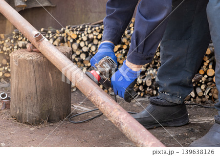 A dedicated worker uses an electric angle grinder to smooth and polish a rusty metal pipe in an outdoor workshop, highlighting industrial craftsmanship, manual labor, and home improvement tasks A dedicated worker uses an electric angle grinder to smooth and polish a rusty metal pipe in an outdoor workshop, highlighting industrial craftsmanship, manual labor, and home improvement tasks 139638126