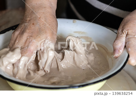An elderly person uses their hands to mix a fresh yeast starter in a white bowl, preparing dough for traditional homemade bread while highlighting artisan culinary techniques today An elderly person uses their hands to mix a fresh yeast starter in a white bowl, preparing dough for traditional homemade bread while highlighting artisan culinary techniques today 139638254