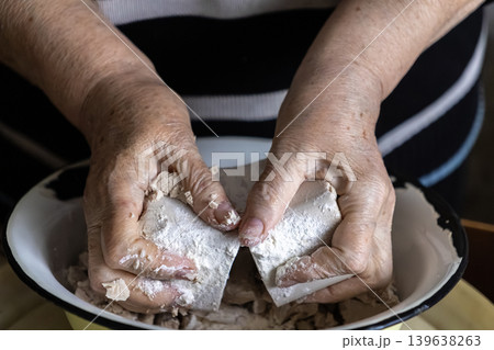 Elderly hands breaking a block of fresh yeast into a bowl, demonstrating traditional baking preparation and sourdough starter cultivation for handmade rustic bread in a kitchen 139638263