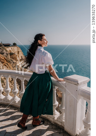 Woman sea terrace happy woman looks at the ocean from a white stone balcony on a sunny summer day during her vacation Woman sea terrace happy woman looks at the ocean from a white stone balcony on a sunny summer day during her vacation 139638270