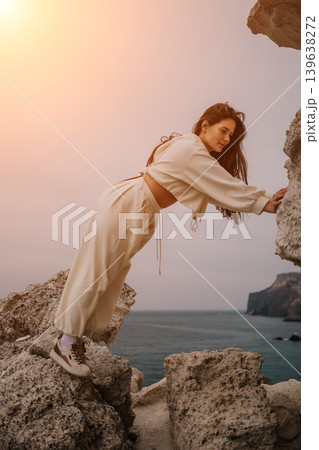 Woman cliffs ocean leaning between rocks while looking at the sea during sunset Woman cliffs ocean leaning between rocks while looking at the sea during sunset 139638272