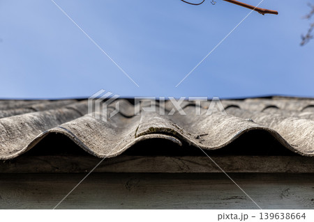 Old corrugated asbestos cement roof tiles against a clear blue sky, illustrating rural construction, home maintenance, housing renovation projects, and classic building materials 139638664