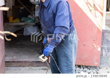 Manual worker in uniform holding old electrical plug outside garage, illustrating maintenance tasks, technical repair services, utility work, professional craftsmanship and labor Manual worker in uniform holding old electrical plug outside garage, illustrating maintenance tasks, technical repair services, utility work, professional craftsmanship and labor 139638690