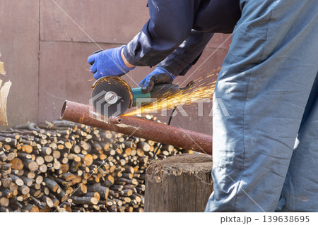 An industrial worker uses an electric angle grinder to cut a heavy metal pipe, creating bright sparks to represent professional construction labor and maintenance in a workshop An industrial worker uses an electric angle grinder to cut a heavy metal pipe, creating bright sparks to represent professional construction labor and maintenance in a workshop 139638695